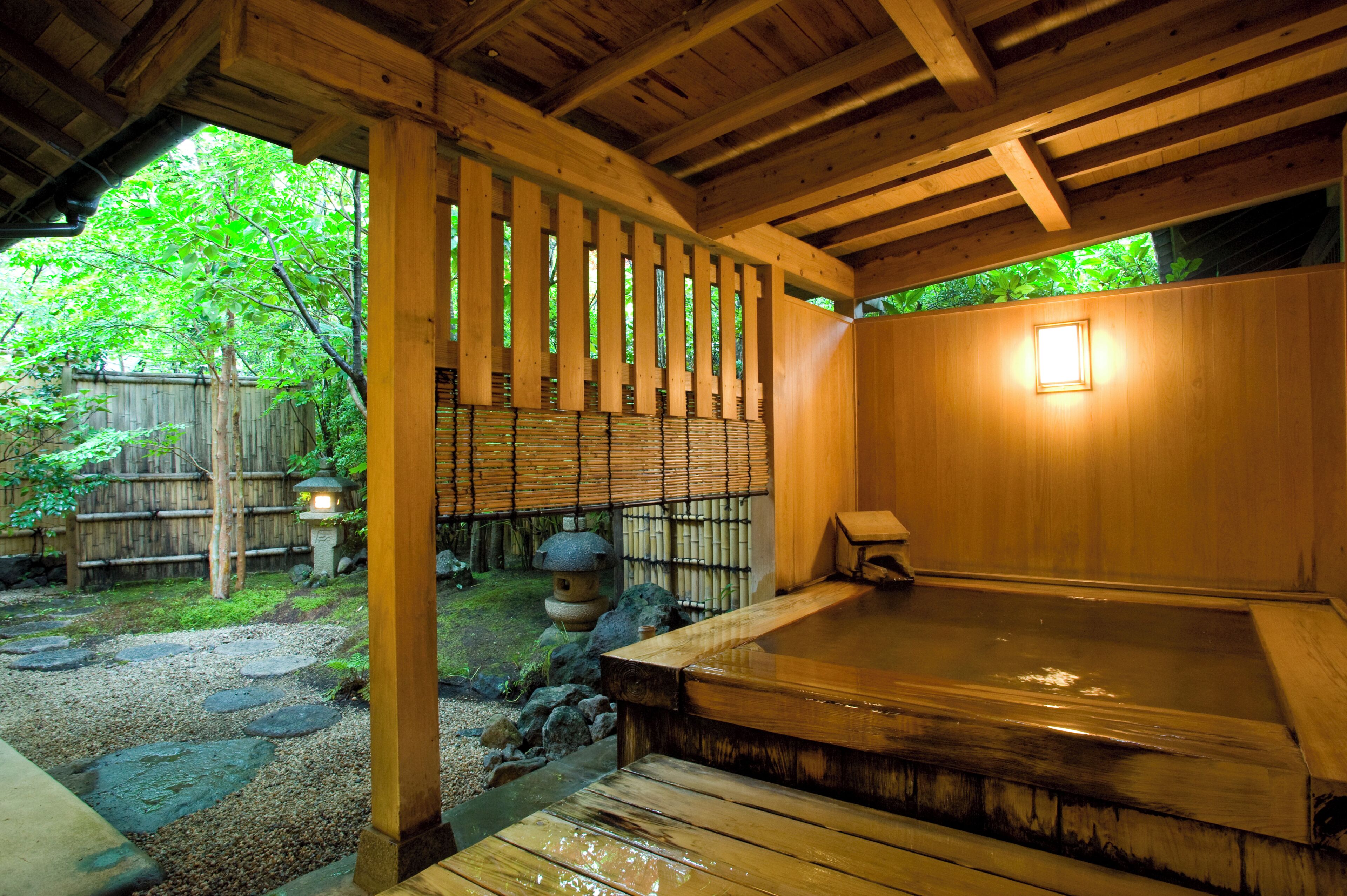 A traditional wooden bathhouse with a hot spring, wooden beams, and a bamboo fence.