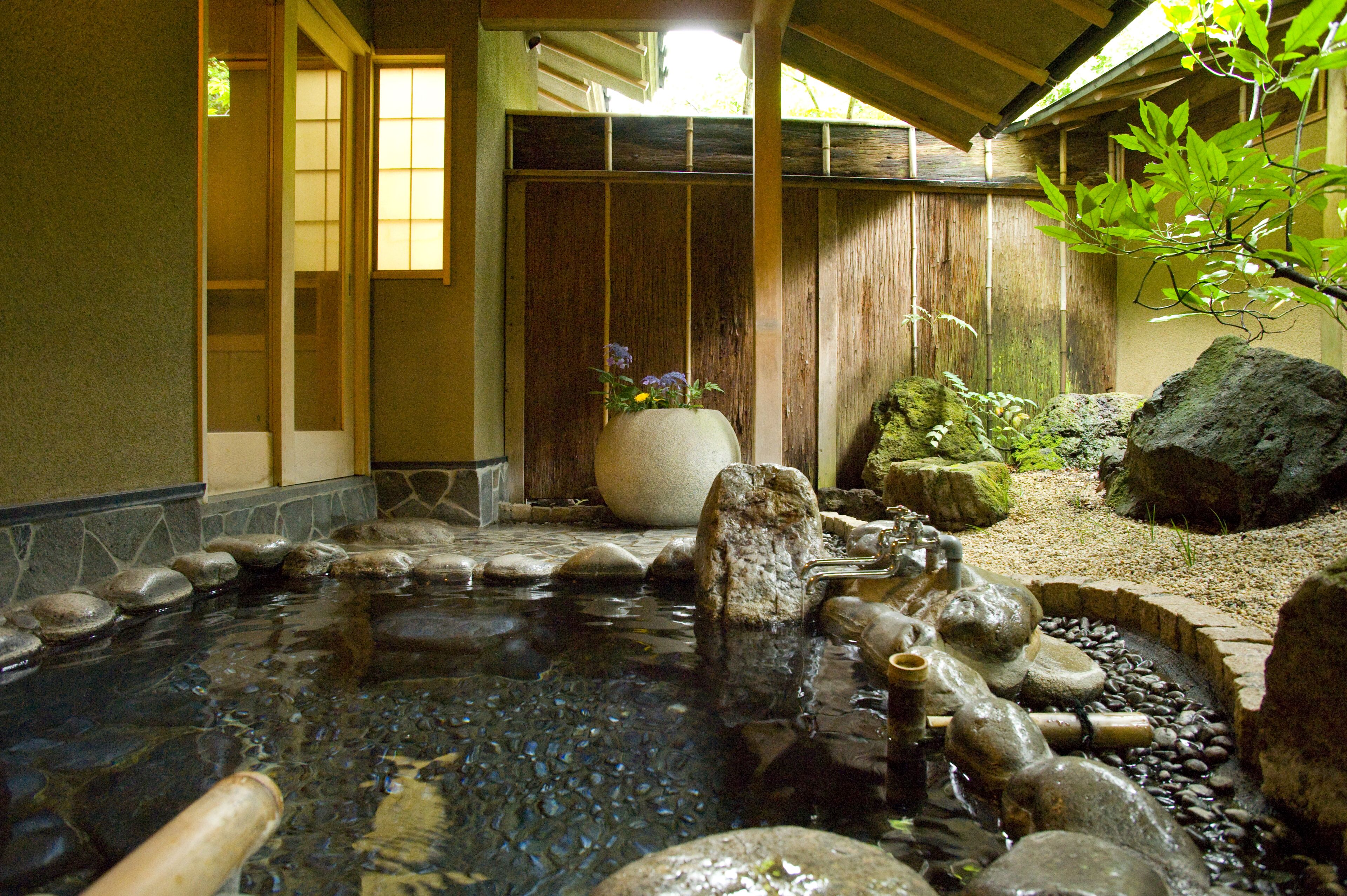 A traditional Japanese garden with a koi pond, rocks, and a wooden fence.