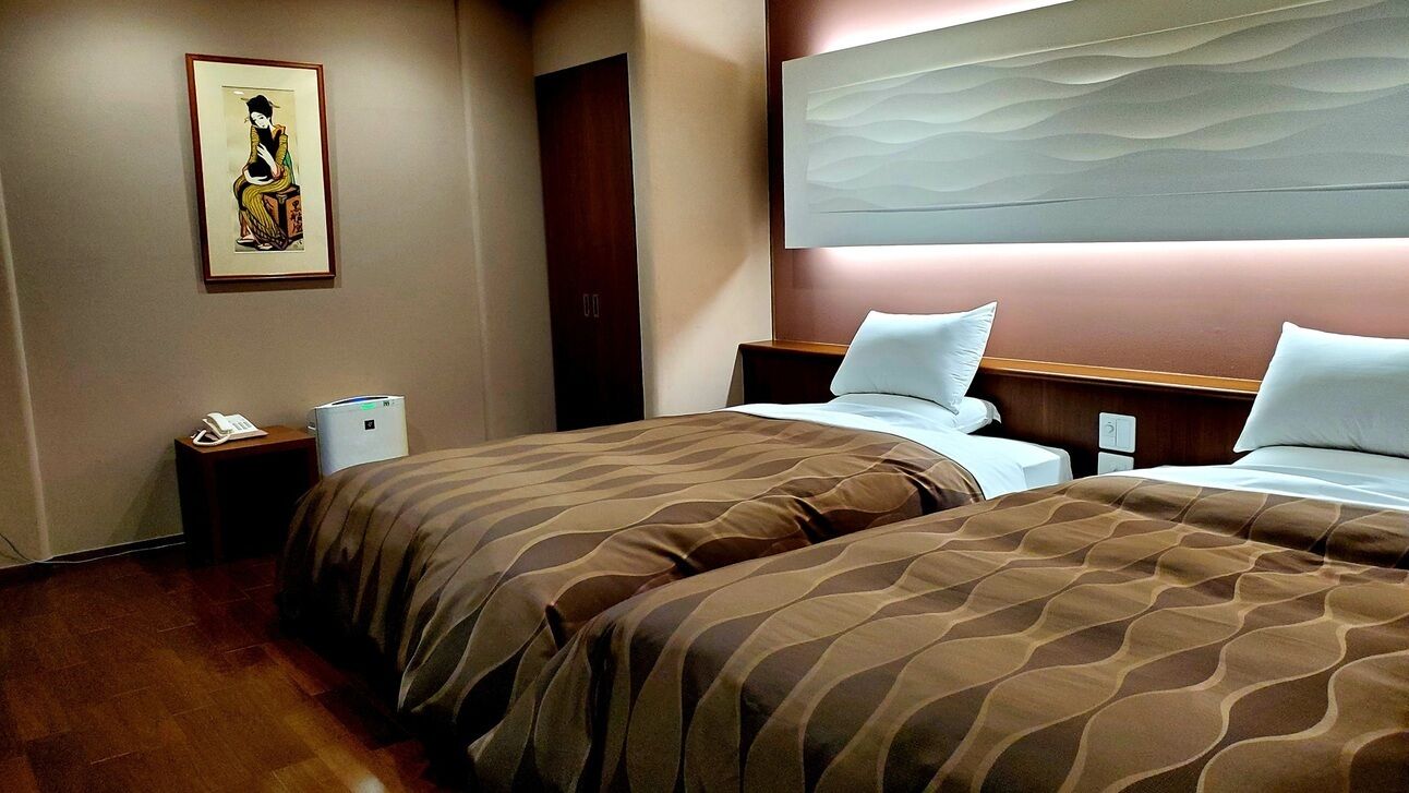 Habitación de hotel con dos camas, una mesita de noche con teléfono, una obra de arte en la pared y un cabecero de madera.