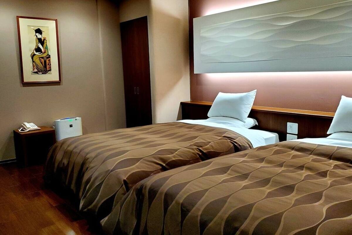 Ein Hotelzimmer mit zwei Betten, einem Nachttisch mit Telefon, einem an der Wand befestigten Kunstwerk und einem Holzkopfteil.