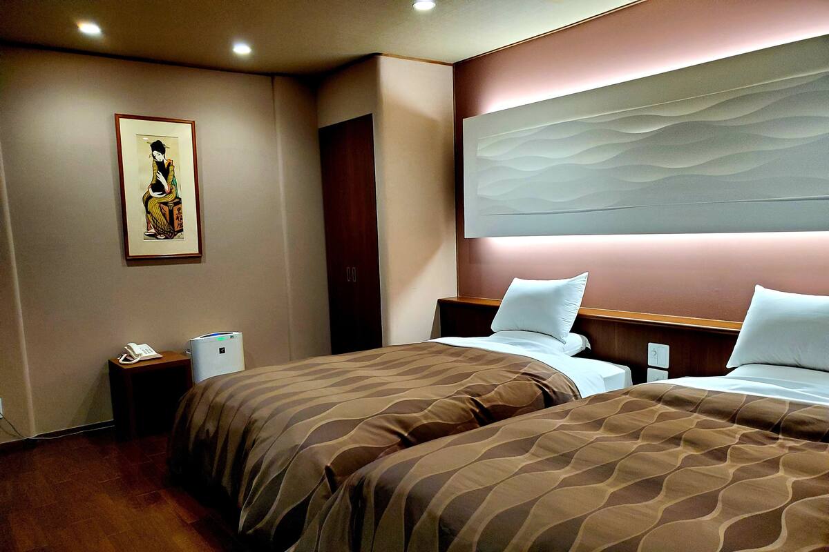 Ein Hotelzimmer mit zwei Betten, einem großen abstrakten Gemälde an der Wand, einem Telefon und einem Mülleimer.