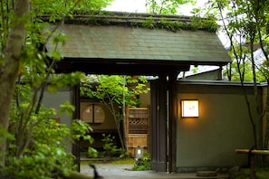 Perinteinen japanilainen rakennus, jossa on olkikatto, pieni valaistu kyltti ja kivipolku, joka johtaa sisäänkäynnille.