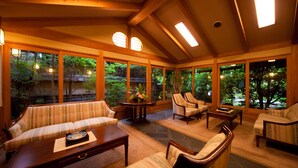 Ein geräumiger Raum mit hoher Decke, großen Fenstern und Holzbalken. Es gibt mehrere Sitzbereiche mit Sofas und Sesseln.