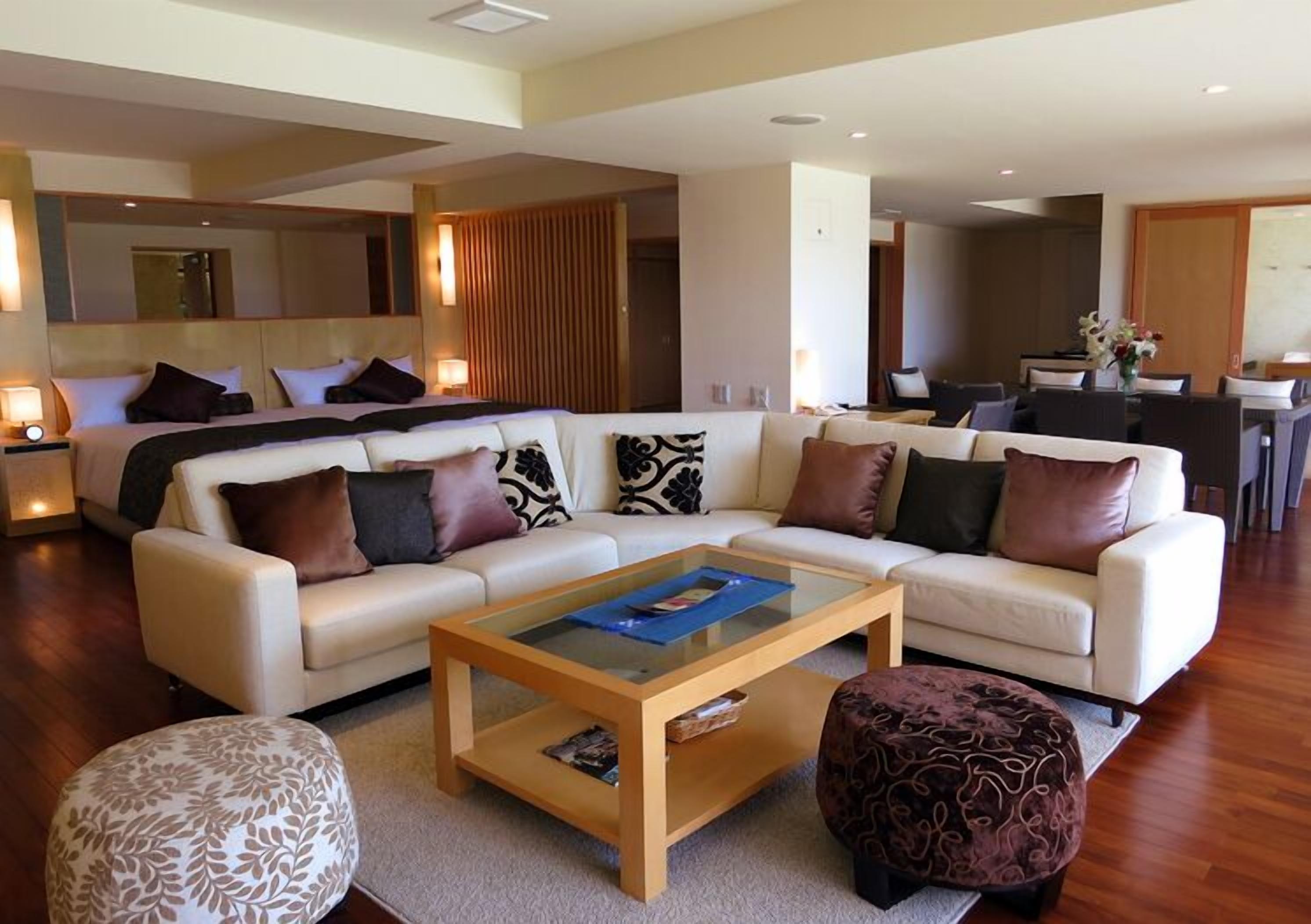A modern living room with a sofa, ottoman, coffee table, and a dining area in the background.