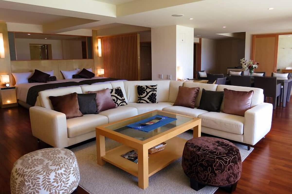 Una sala de estar moderna con sofá, reposapiés, mesa de centro y una zona de comedor al fondo.