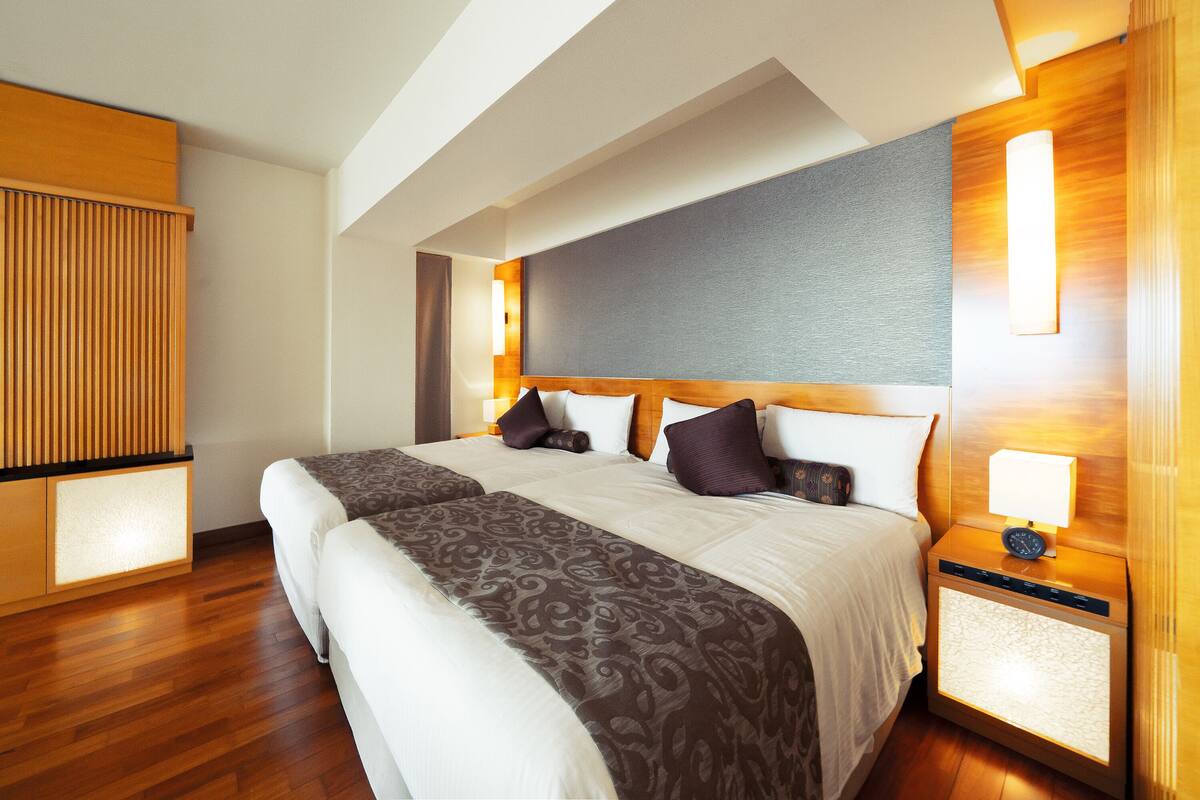 Habitación de hotel con una cama grande, dos mesitas de noche, un velador con lámpara y un cabecero de madera.