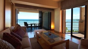 A modern living room with a sofa, coffee table, and a view of the sea through large windows. - Hyakuna Garan (Nanjo)