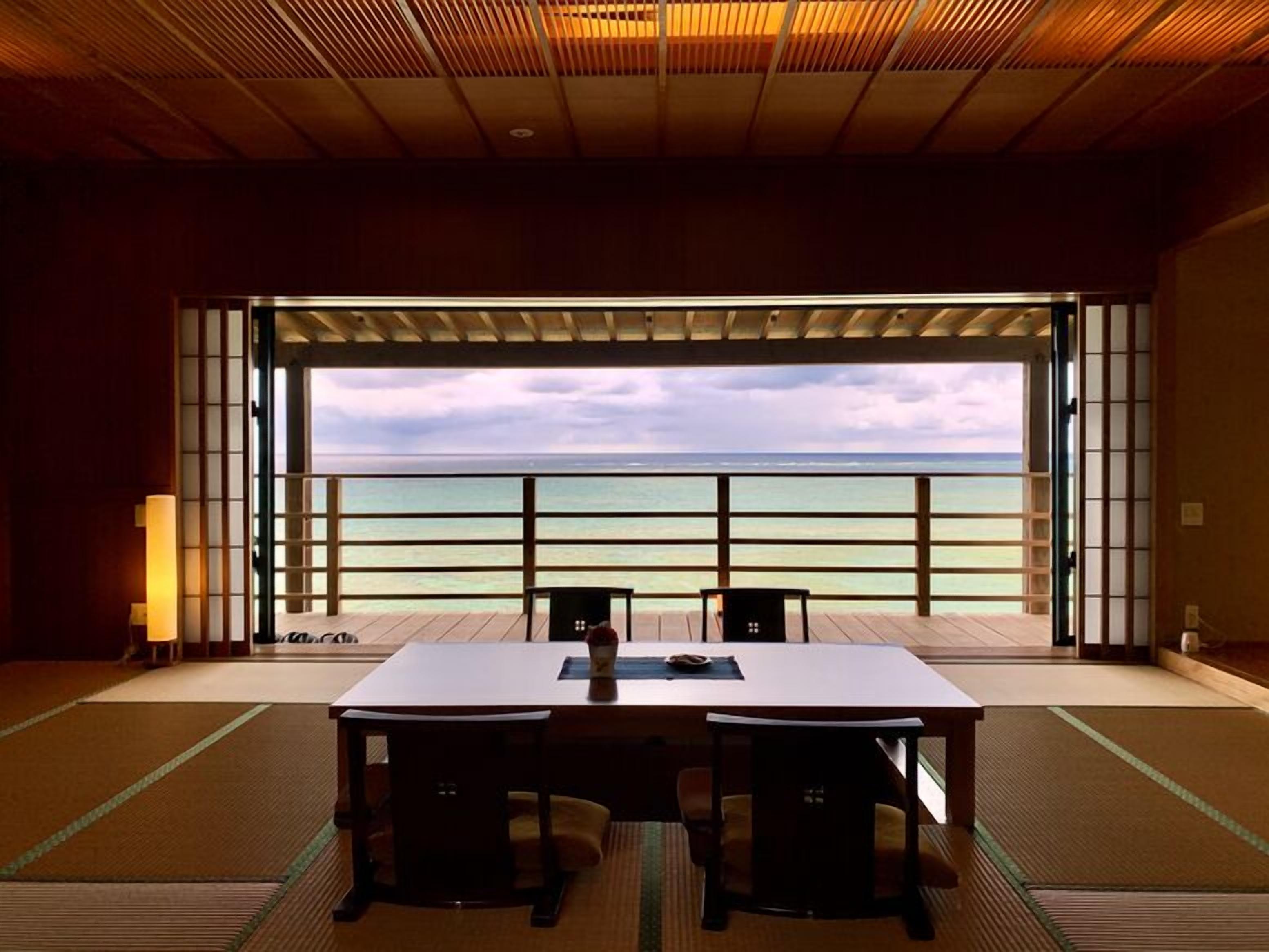 Una habitación con suelo de tatami, una mesa de madera, dos sillas y vistas al océano.
