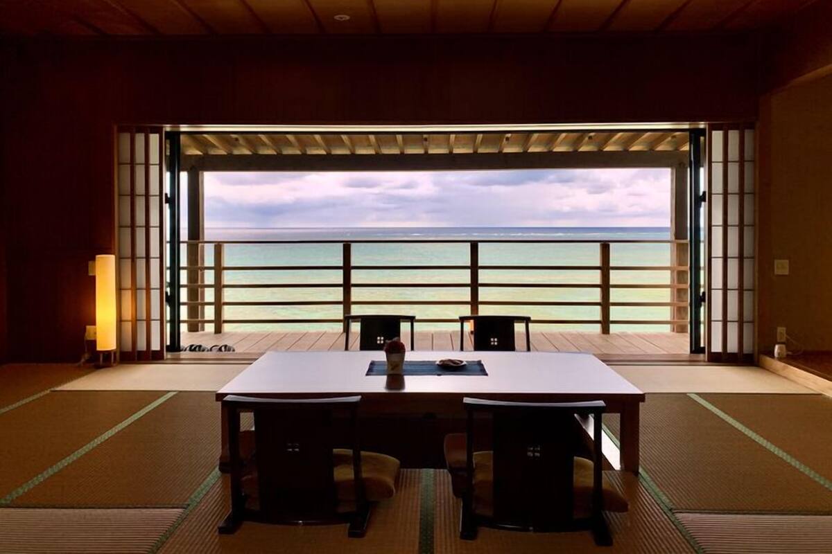 Una habitación con suelo de tatami, una mesa de madera, dos sillas y vistas al océano.