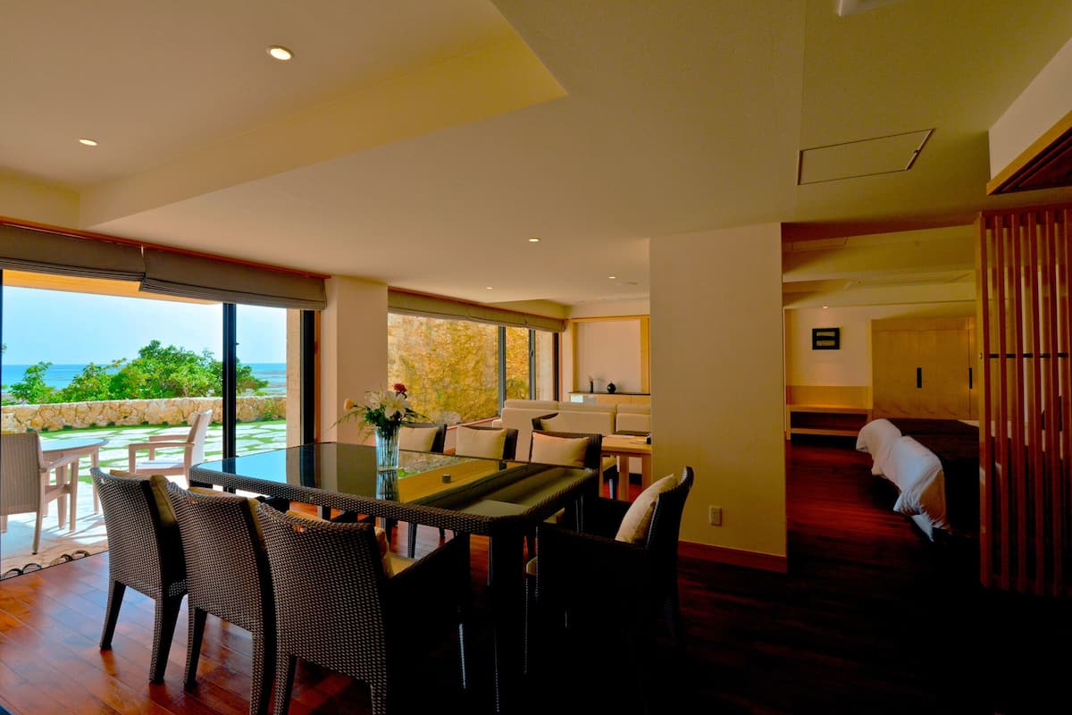 Una habitación amplia con una gran mesa de comedor, sillas de mimbre y vista al océano.