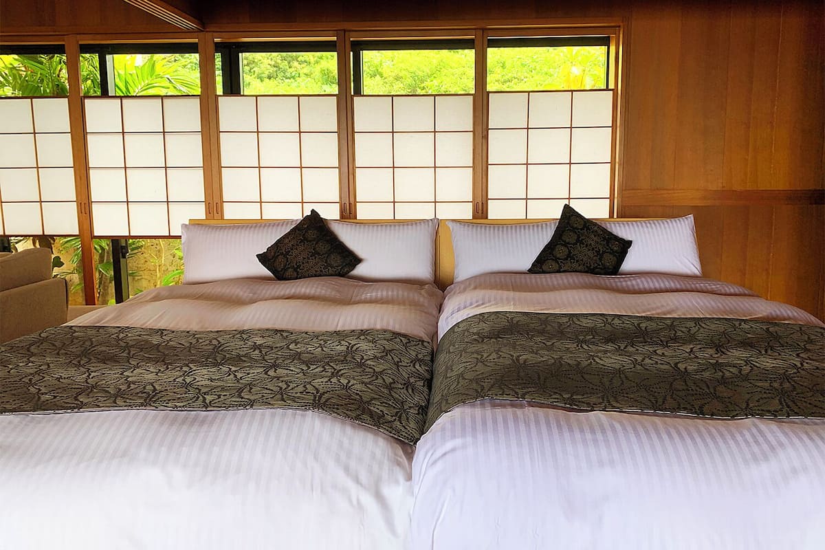 Una cama doble con ropa de cama estampada, un cabecero de madera y vistas a la vegetación a través de un panel shoji.