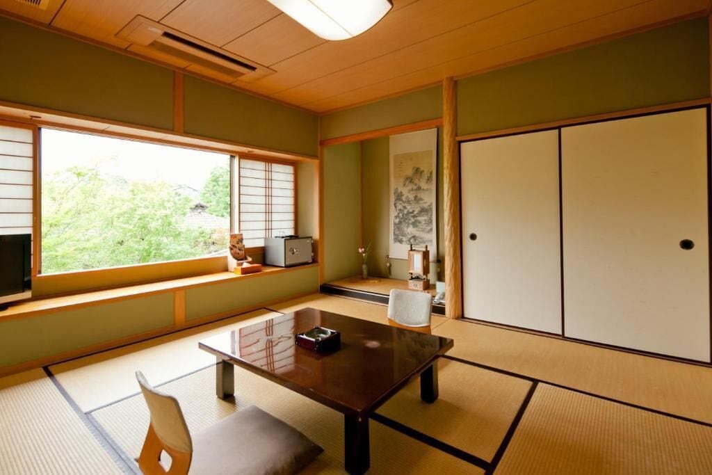 A traditional Japanese room with tatami flooring, a low table, a sliding door, and a view of greenery outside.