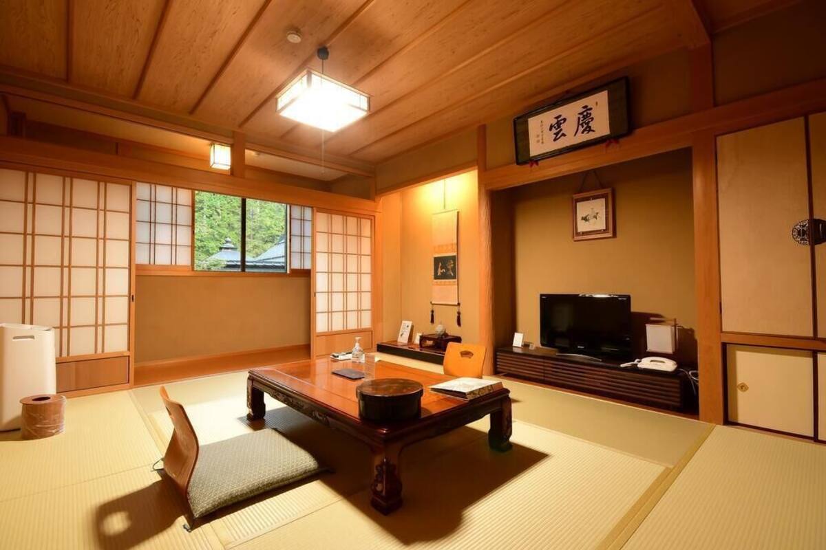 A traditional Japanese room with tatami flooring, a low table, a television, and sliding doors.