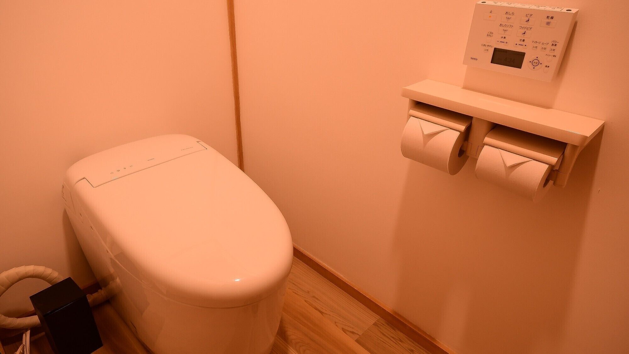 A toilet with a wall-mounted toilet paper holder and a visible pipe.
