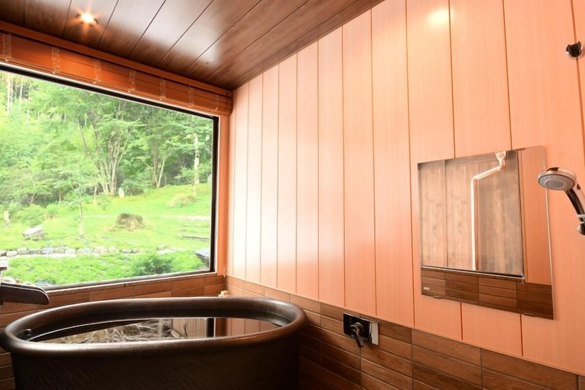 Un baño con paneles de madera, una bañera de hidromasaje, una ventana con vistas al bosque y una ducha.