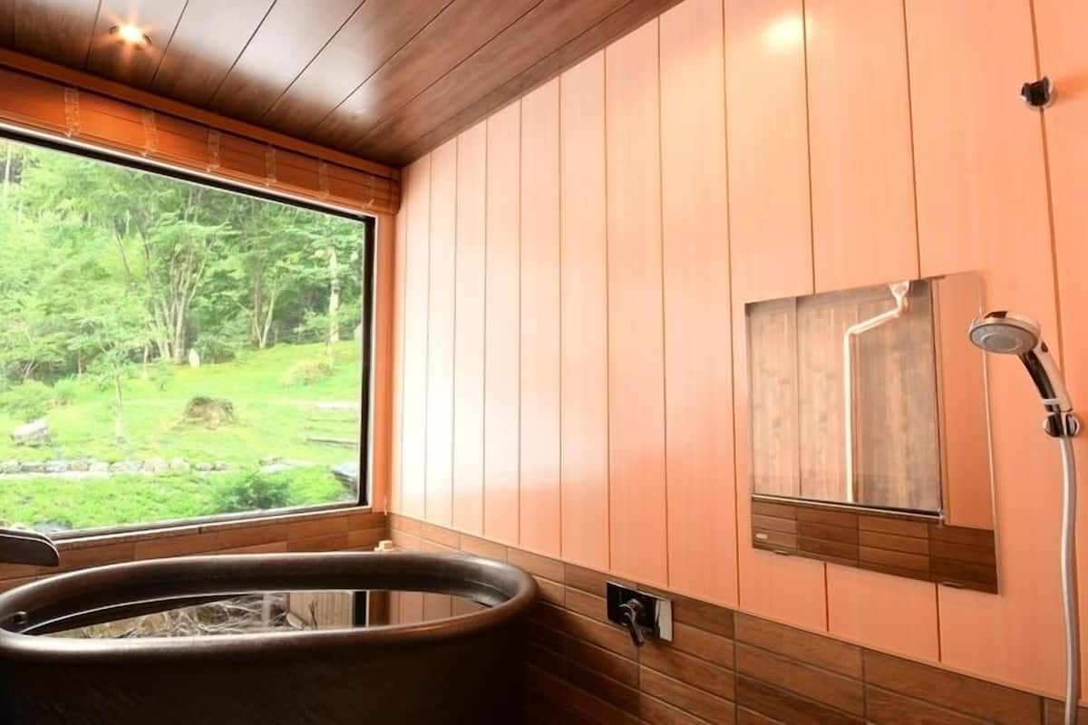 A wooden-paneled bathroom with a hot tub, a window with a forest view, and a shower.