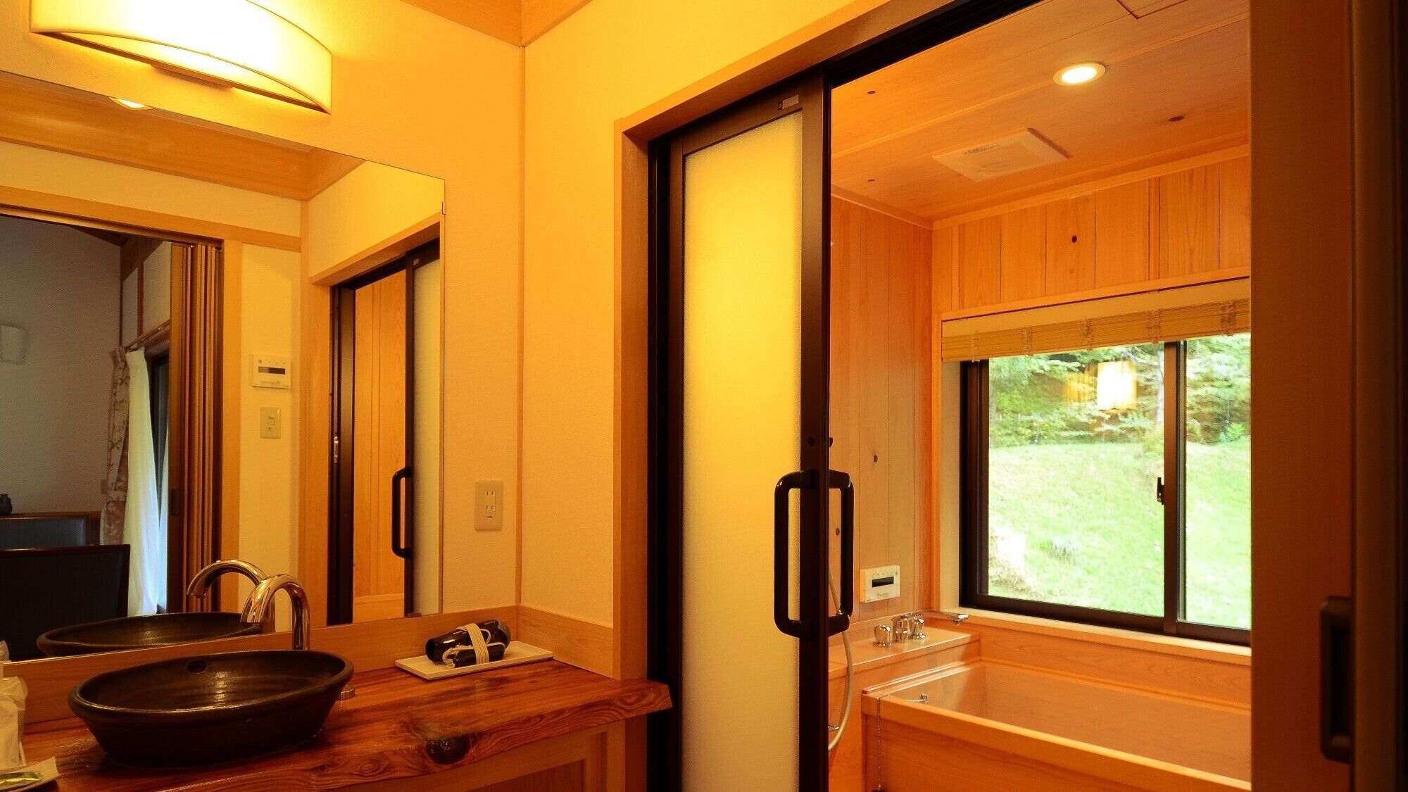 A bathroom with a wooden vanity, a large mirror, a black basin, and a window with a view of greenery.