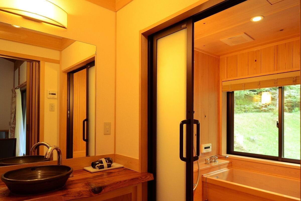 A bathroom with a wooden vanity, a large mirror, a black basin, and a window with a view of greenery.