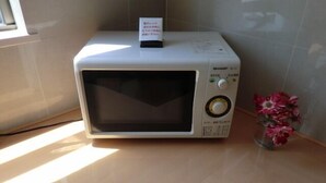 Un four à micro-ondes posé sur un plan de travail de cuisine, avec un petit panneau placé au-dessus.