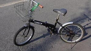 Un vélo d’appartement doté d’un panier à l’avant et d’un porte-bagages à l’arrière, garé sur une surface pavée.