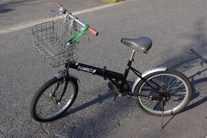 Una bicicleta estática con una cesta delantera y un portaequipajes trasero, estacionada sobre una superficie pavimentada.