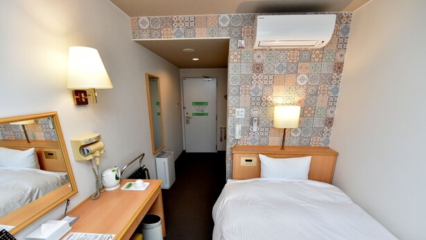 Une chambre d’hôtel avec deux lits, un bureau avec une lampe, un miroir, un sèche-cheveux, une poubelle et un climatiseur fixé au mur.