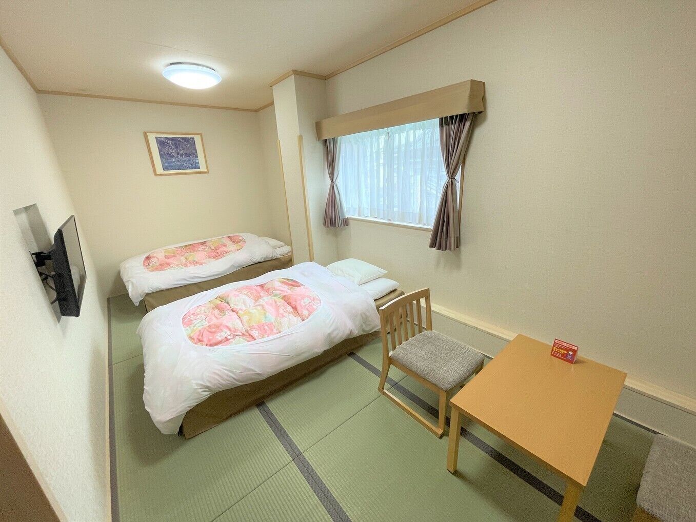A hotel room with two beds, a desk, a chair, a television, and a window with curtains.