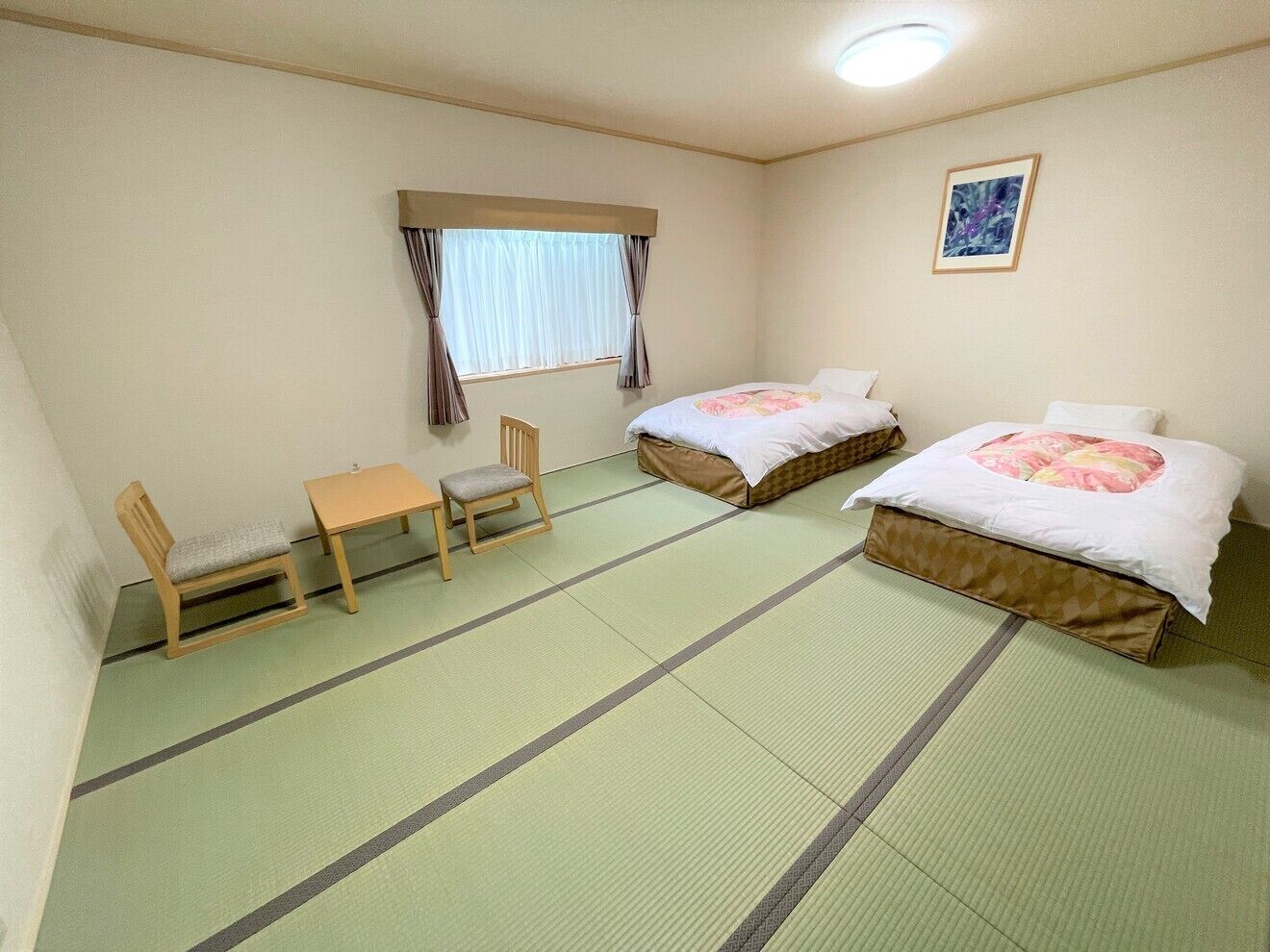 A room with two beds, a chair, a table, and a window with curtains.
