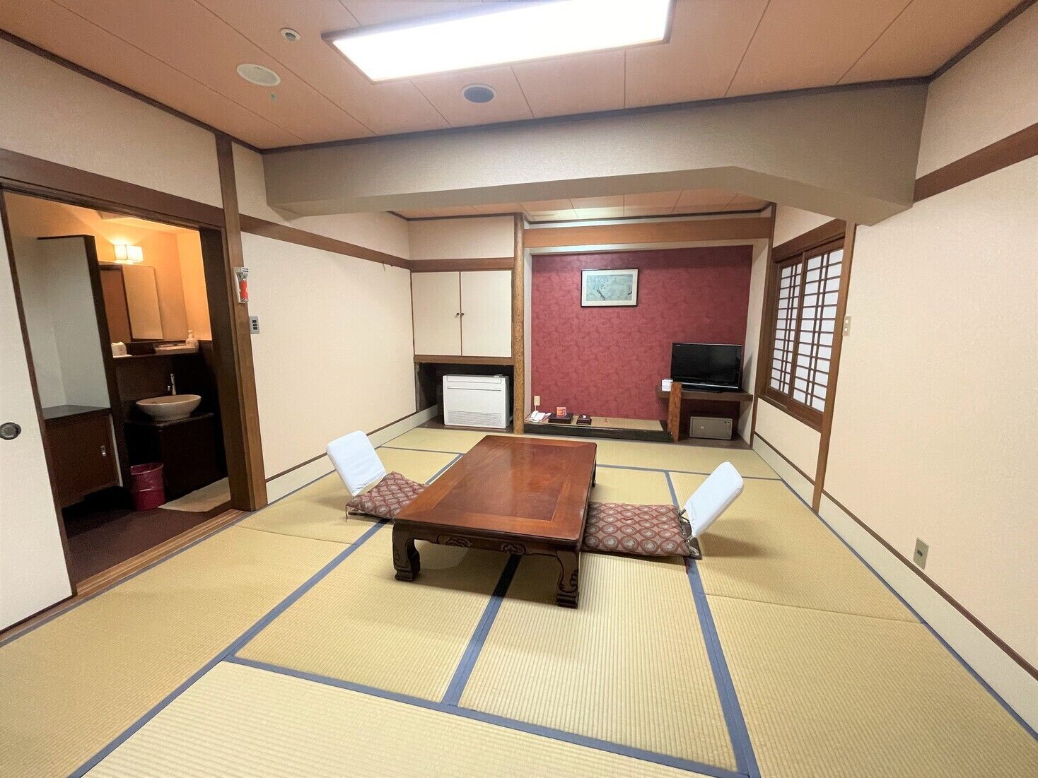 A traditional Japanese room with tatami flooring, a wooden table, two chairs, a television, and a small cabinet.