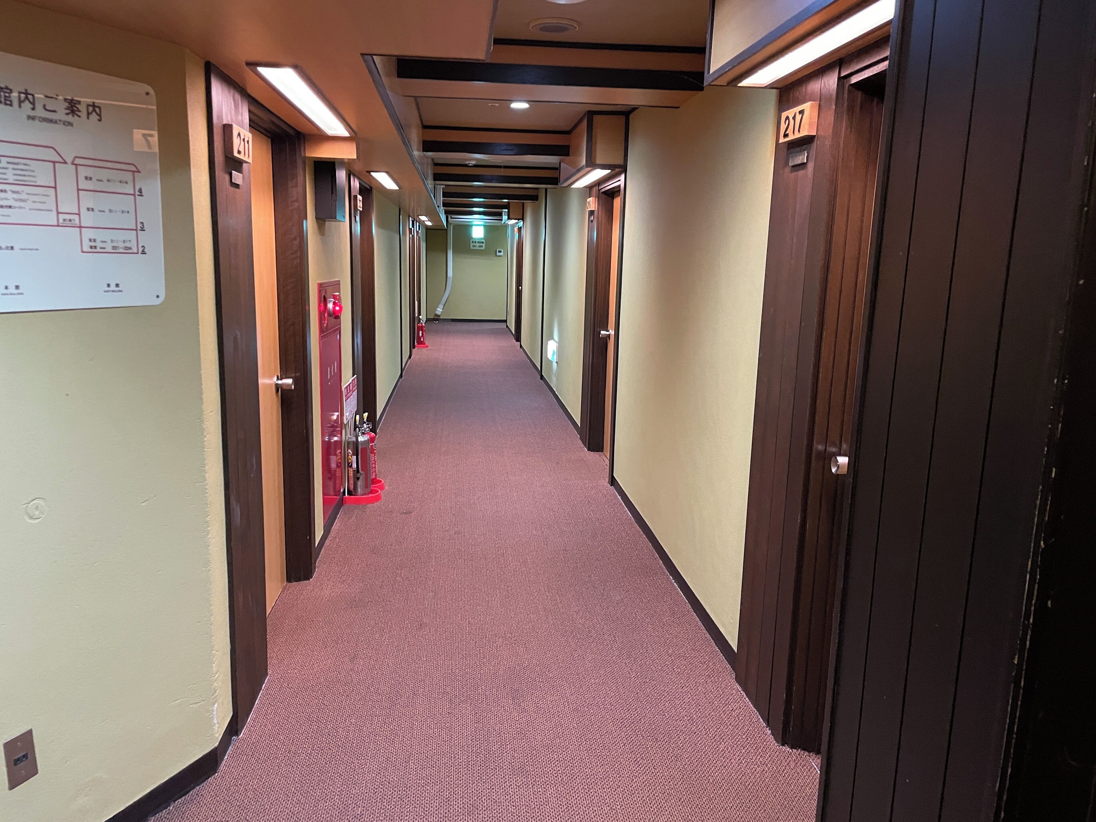 Pasillo de hotel con puertas numeradas, extintor y un panel informativo.