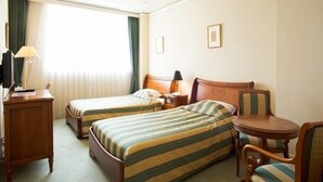 A hotel room with two single beds, a desk with a lamp, a chair, a small table, and a window with curtains. - Hotel Marital Sousei Kurume (Kurume)