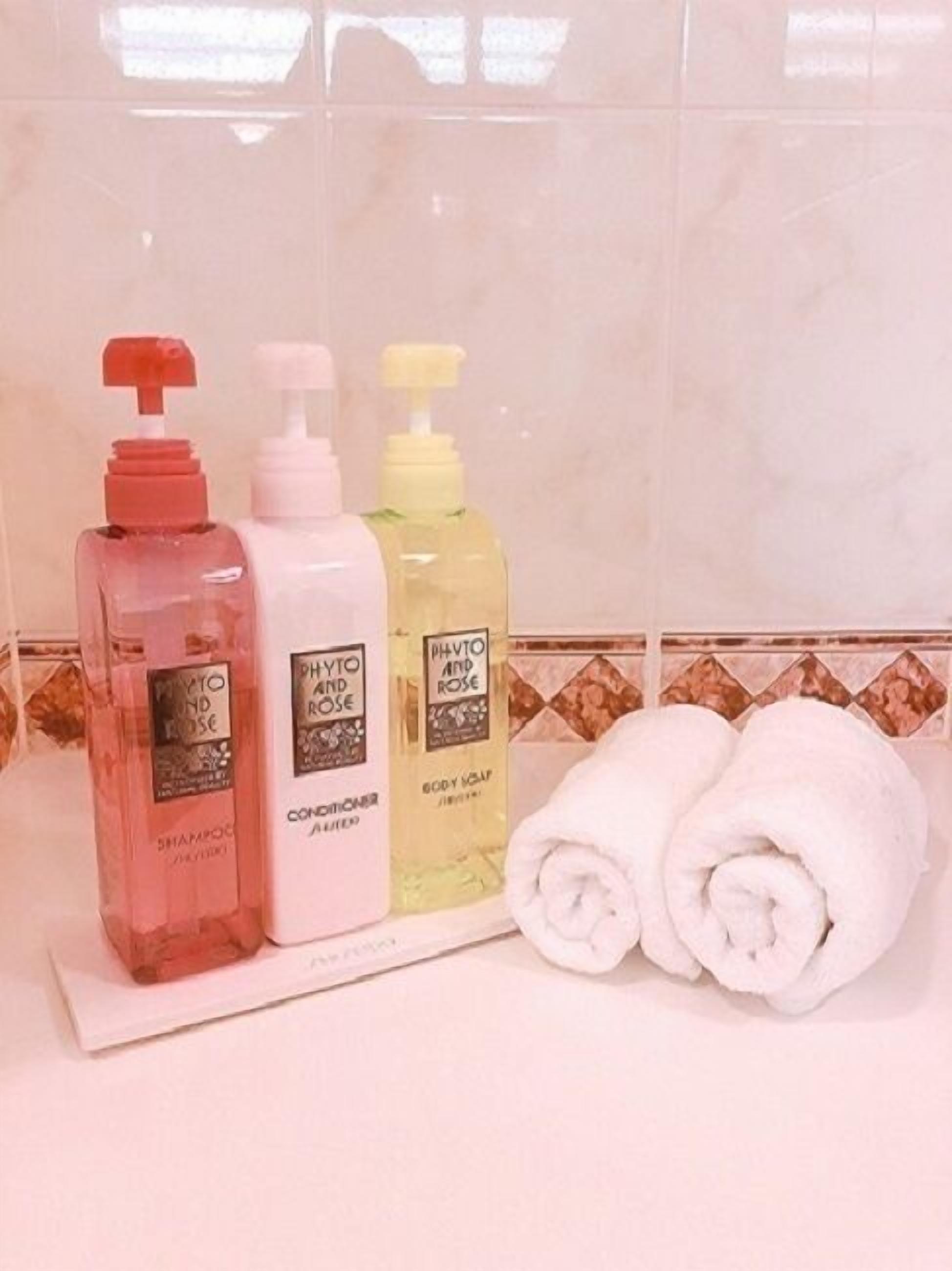 Tres botellas de productos para el cuidado corporal y dos toallas enrolladas sobre una encimera de baño.