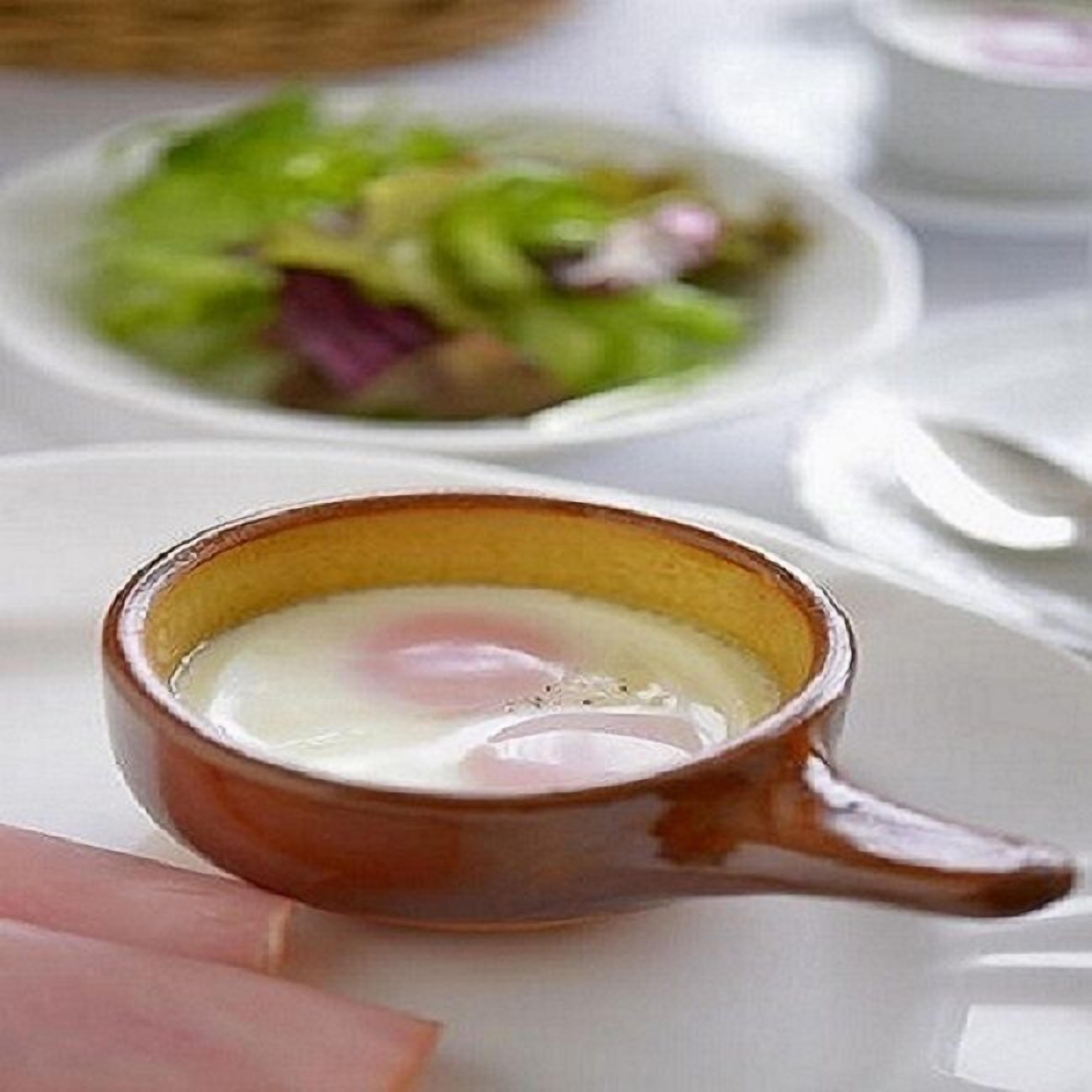 Une petite tasse en céramique avec une anse, contenant un liquide transparent, peut-être une boisson ou une soupe, posée sur une assiette blanche.