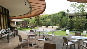 An outdoor patio area with round tables and chairs, a covered seating area, and a view of a garden and building in the background. - Hotel Marital Sousei Kurume (Kurume)
