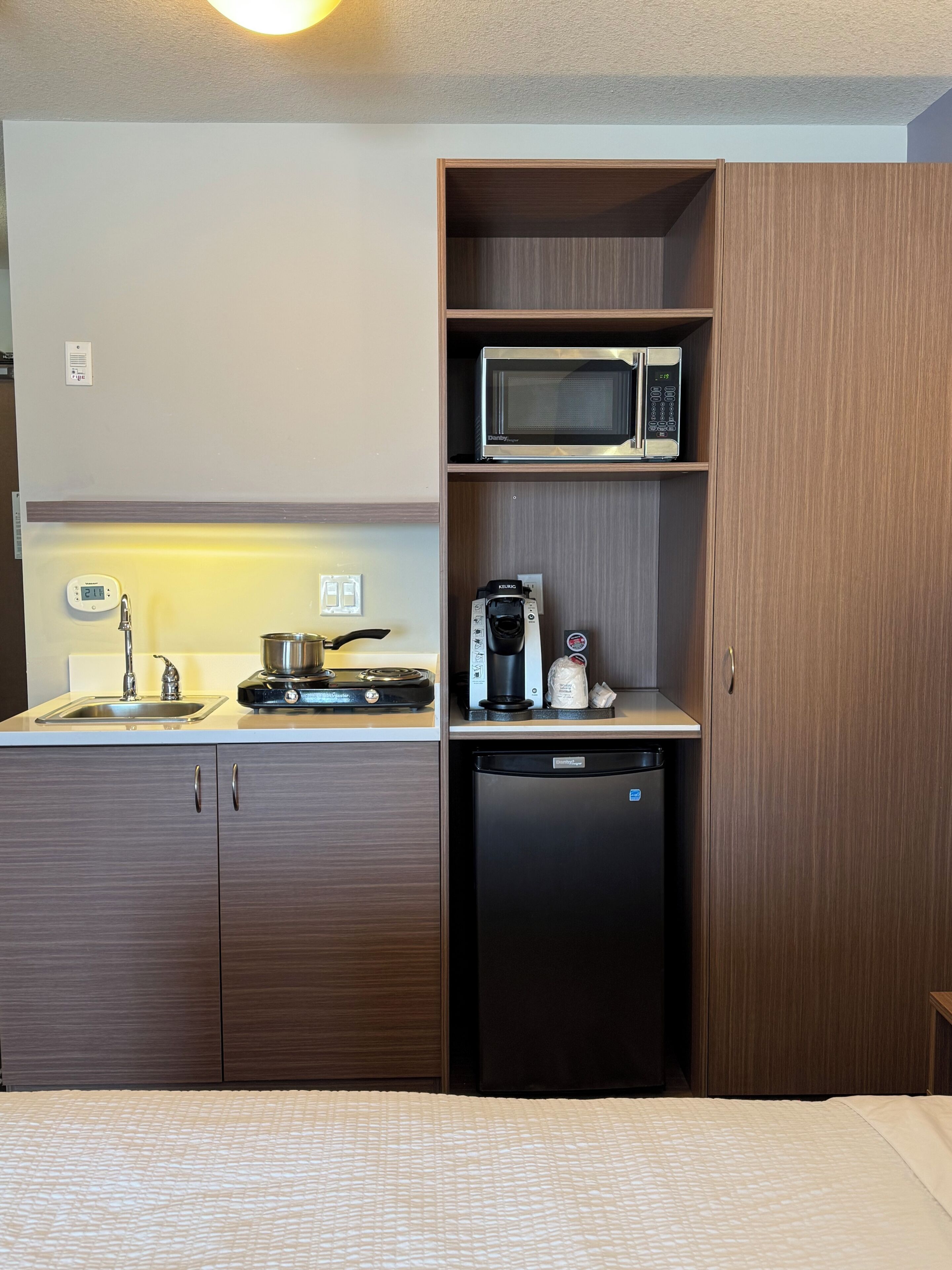 Una kitchenette compacta con microondas, cafetera y un refrigerador pequeño.