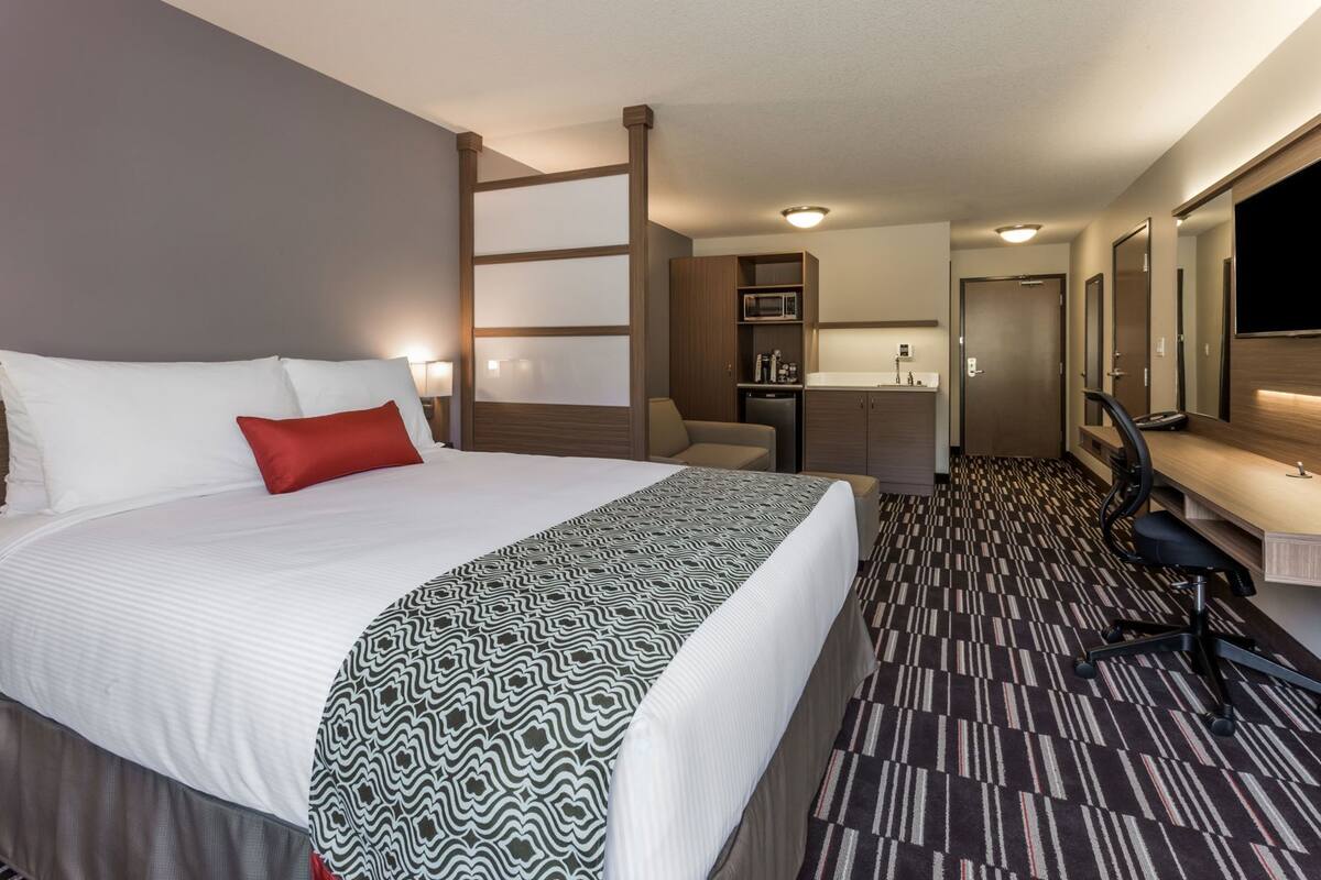 A hotel room with a large bed, a desk, a chair, a kitchenette, and a bathroom.