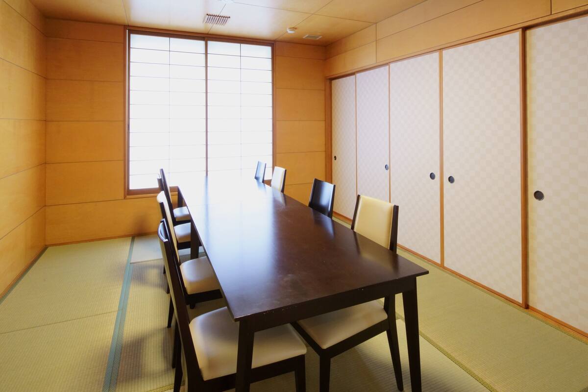 A conference room with a long table, chairs, tatami mats, sliding doors, and a large window.