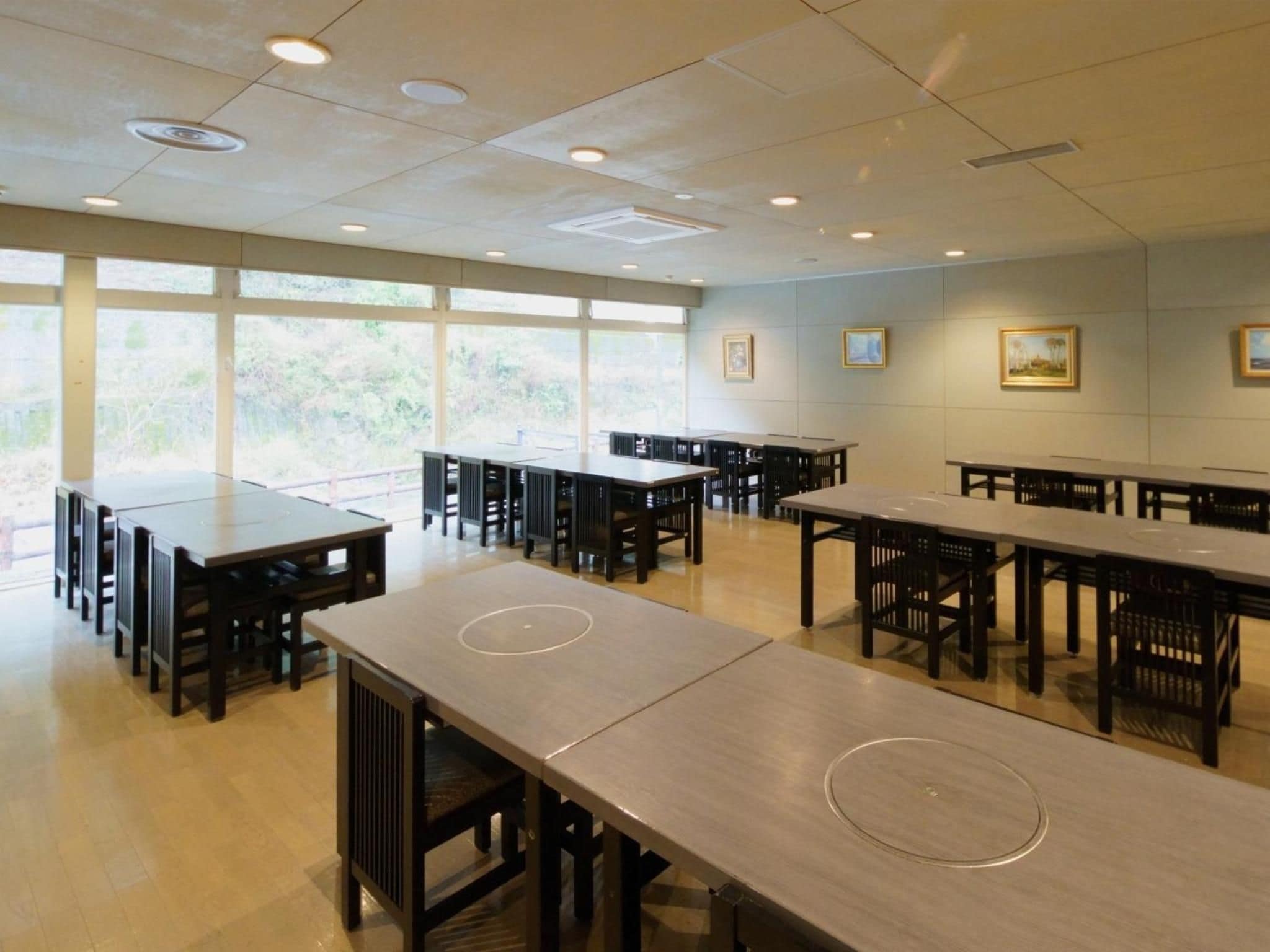 A spacious dining area with multiple tables and chairs, large windows allowing natural light, and framed artwork on the walls.