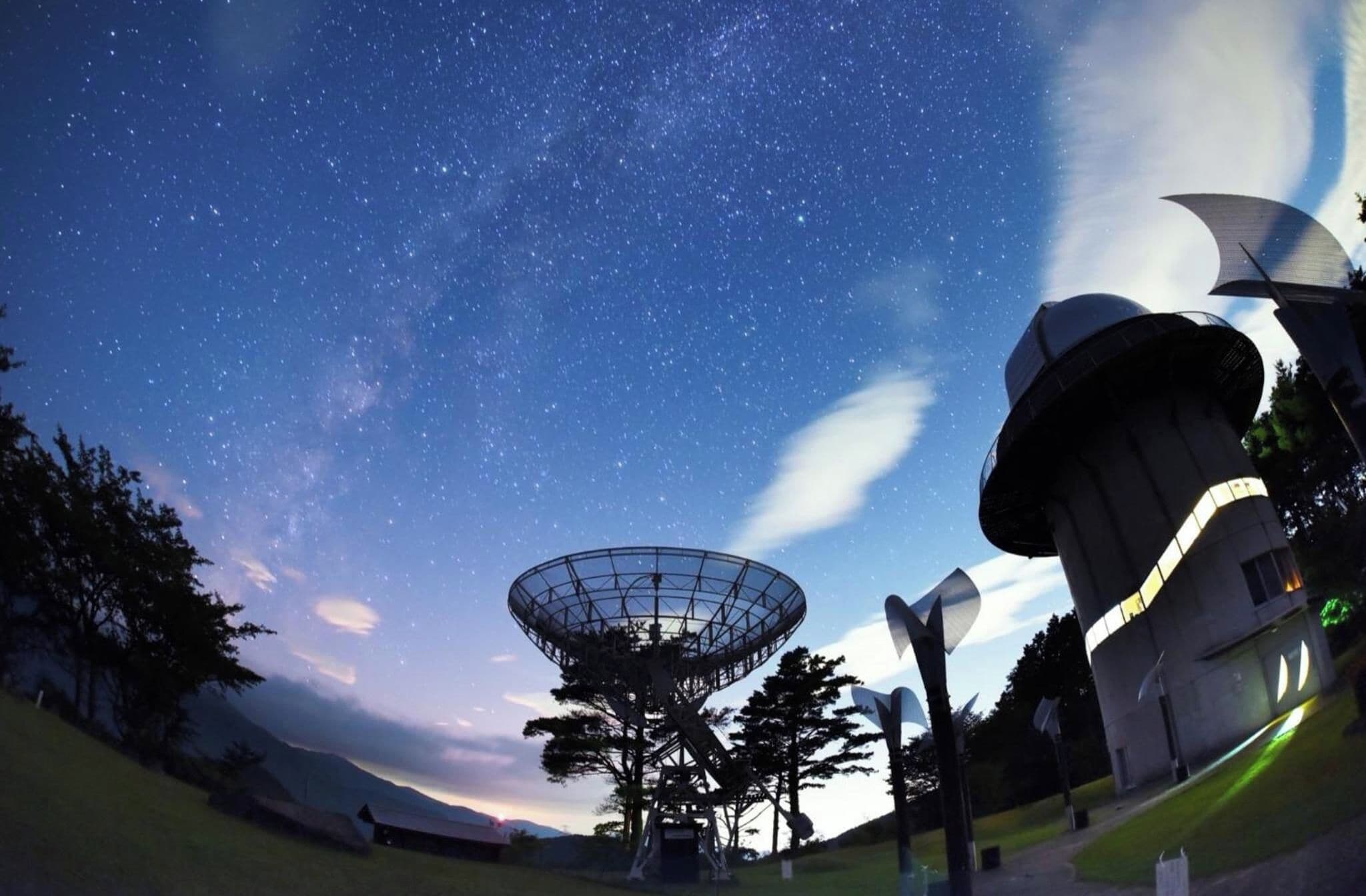 A large telescope structure with a dome, surrounded by trees and a clear night sky.