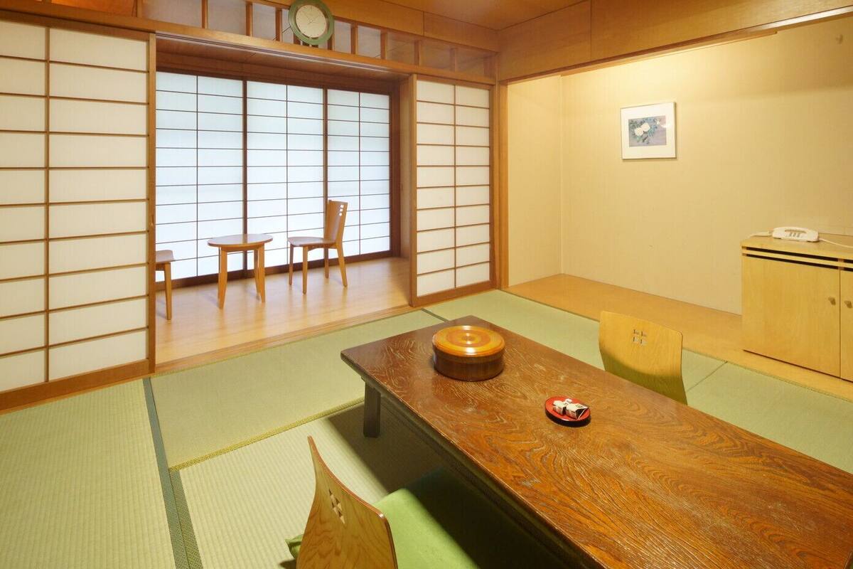 A traditional Japanese room with tatami flooring, a low table with a decorative bowl, a wooden cabinet, and a window with shoji screens.