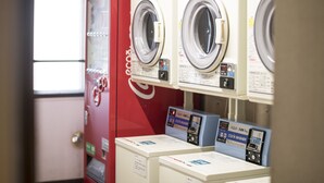 A laundry facility with multiple washing machines and dryers, including a red machine and a blue machine with a digital display. - Hashimoto Park Hotel (Sagamihara)
