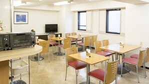 A dining area with multiple tables and chairs, a television, and a trash bin. - Hashimoto Park Hotel (Sagamihara)