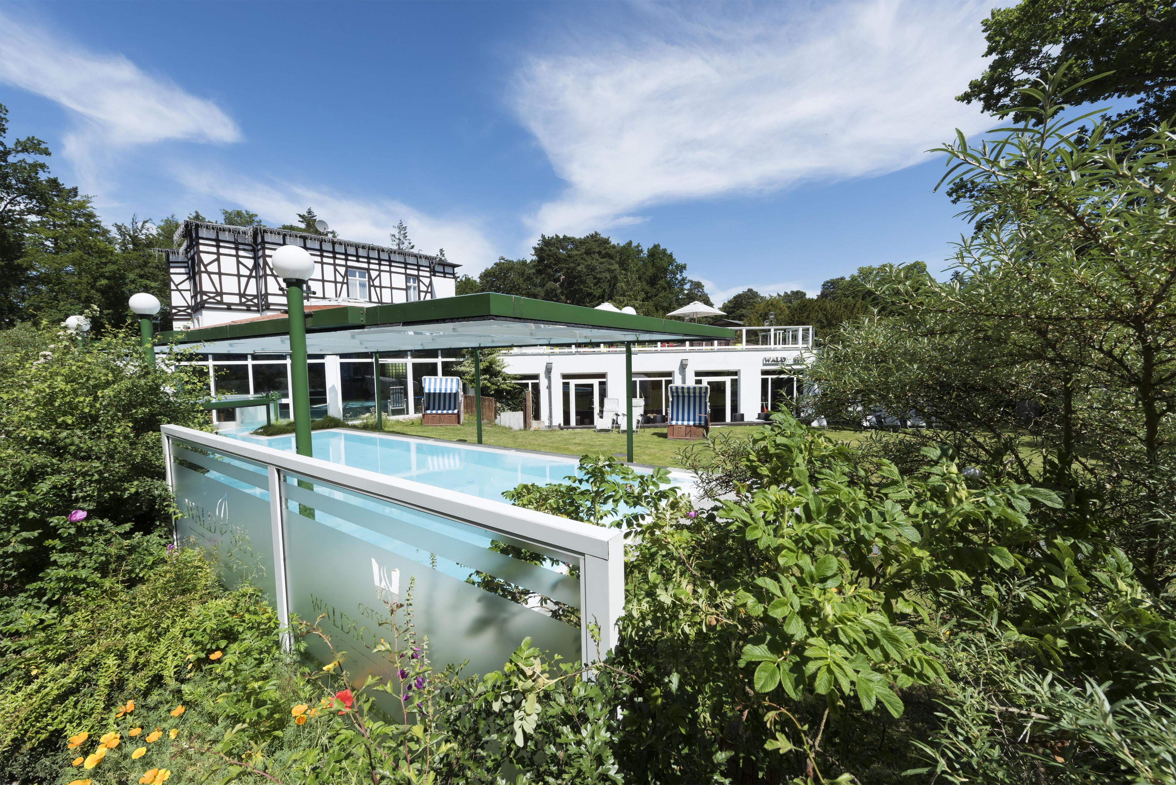 A hotel with a swimming pool, covered outdoor seating, and lush greenery.