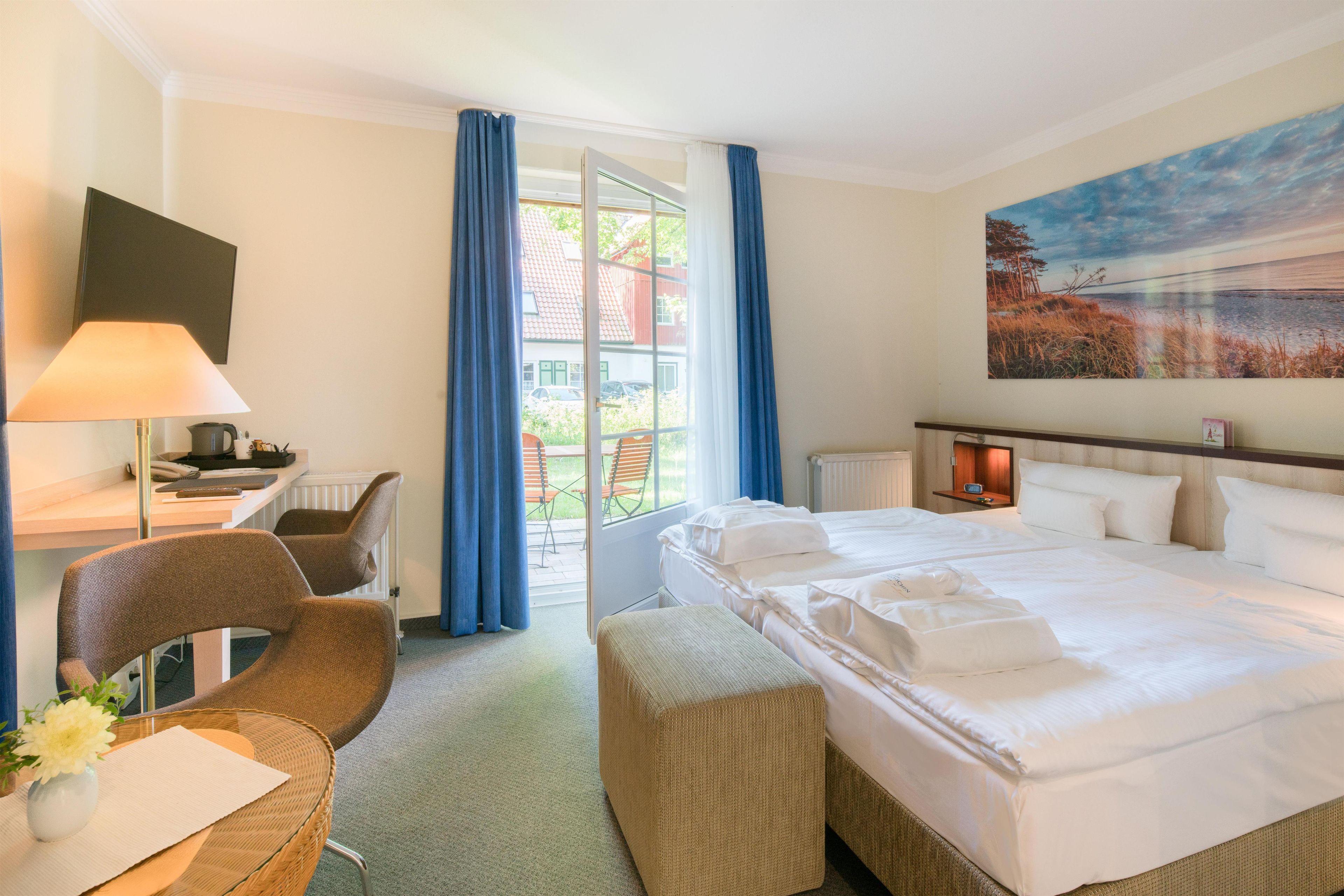 Habitación de hotel con cama, escritorio, silla, lámpara, un cuadro y vistas al exterior.