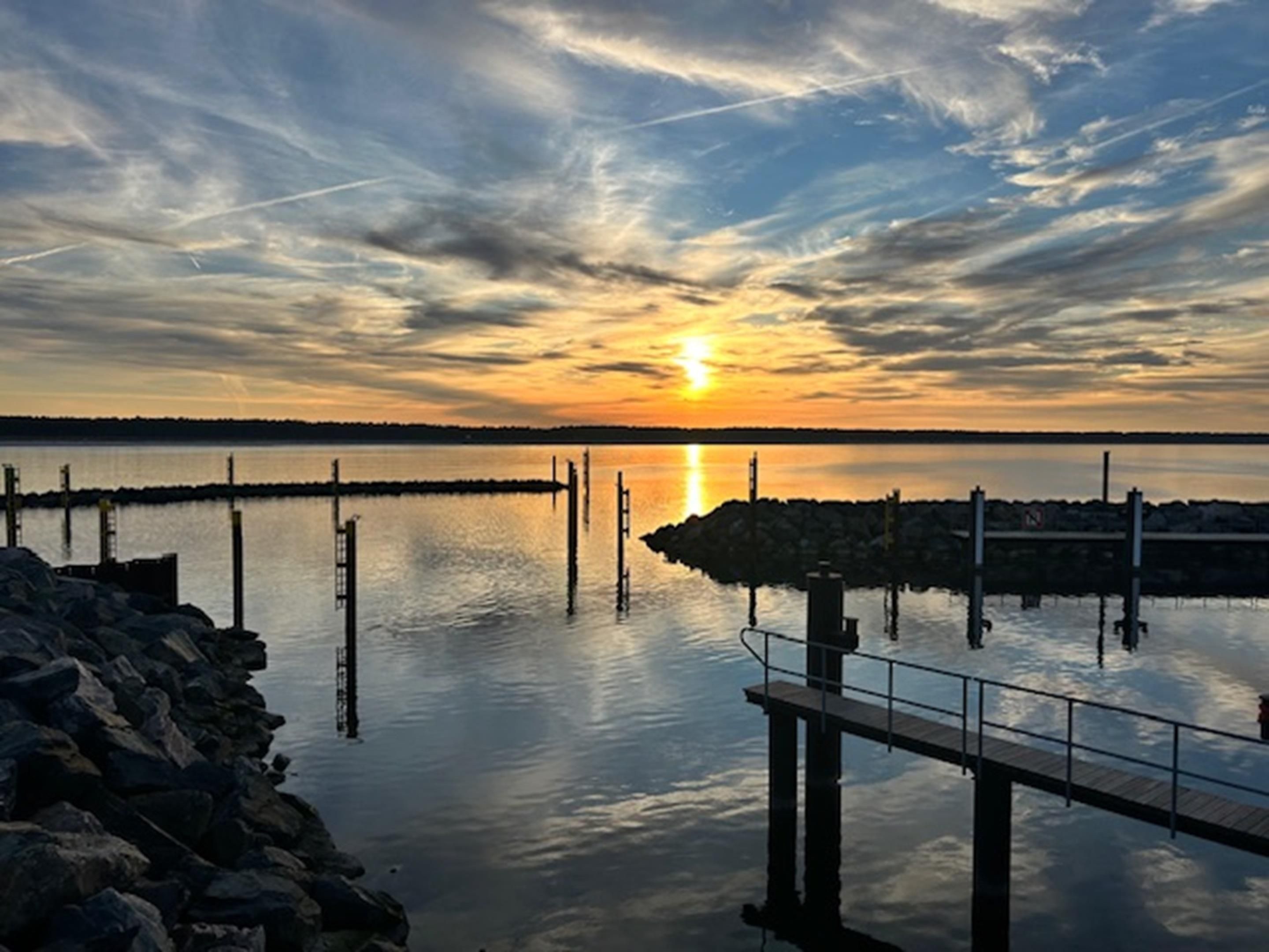 A pier extending into calm water with a sunset in the background.