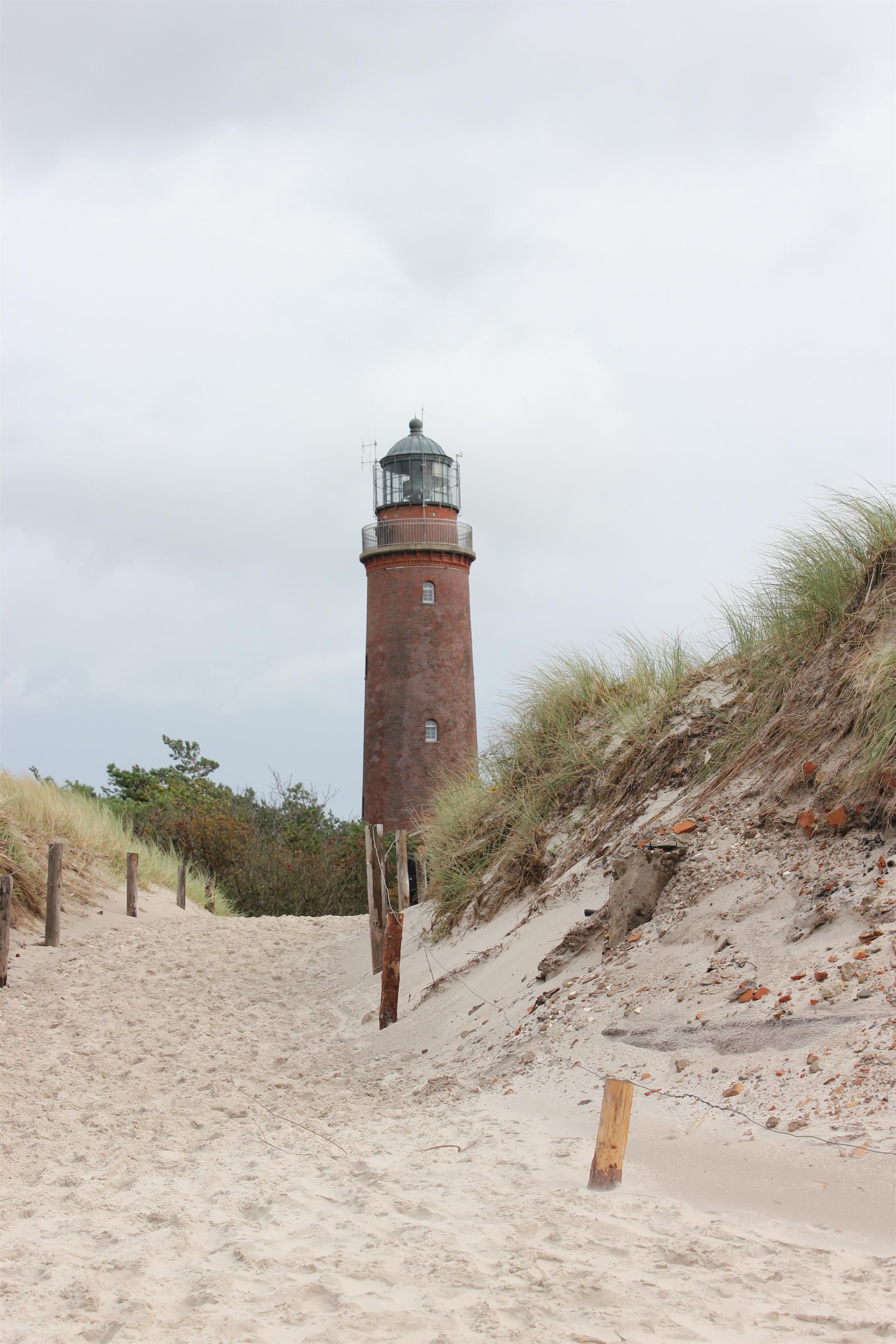 Ein Leuchtturm an einem sandigen Strand mit Holzzaun und Vegetation.