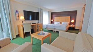 A hotel room with a bed, a desk with a TV, a chair, a small table with a vase, and a sofa. - Best Western Plus Ostseehotel Waldschloesschen (Ostseebad Prerow)