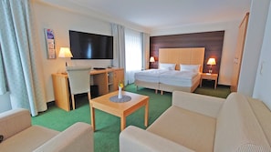 Habitación de hotel con una cama, un escritorio con televisor, una silla, una mesita con un florero y un sofá.