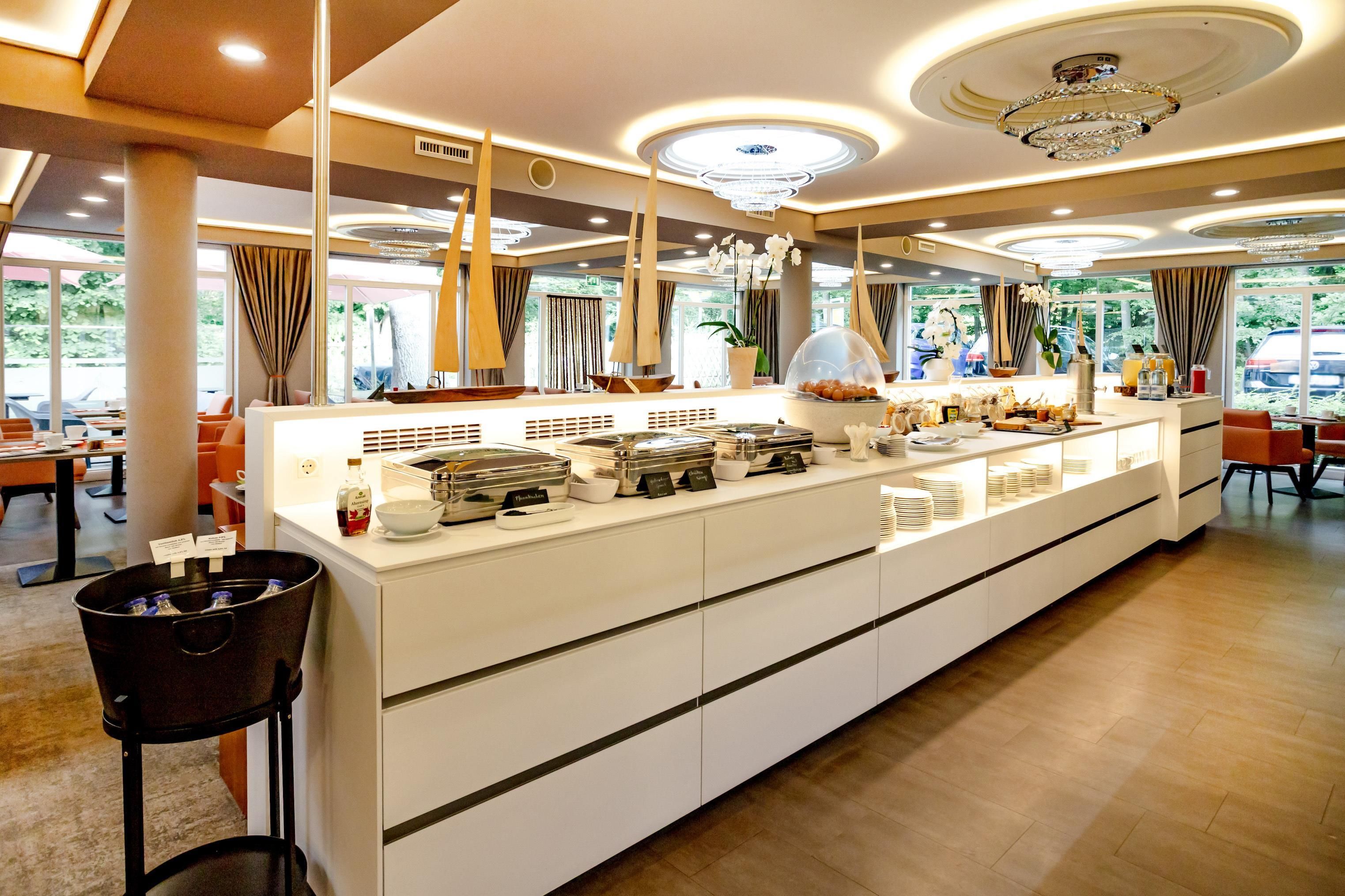A hotel dining area with a buffet setup, a chandelier, and large windows.