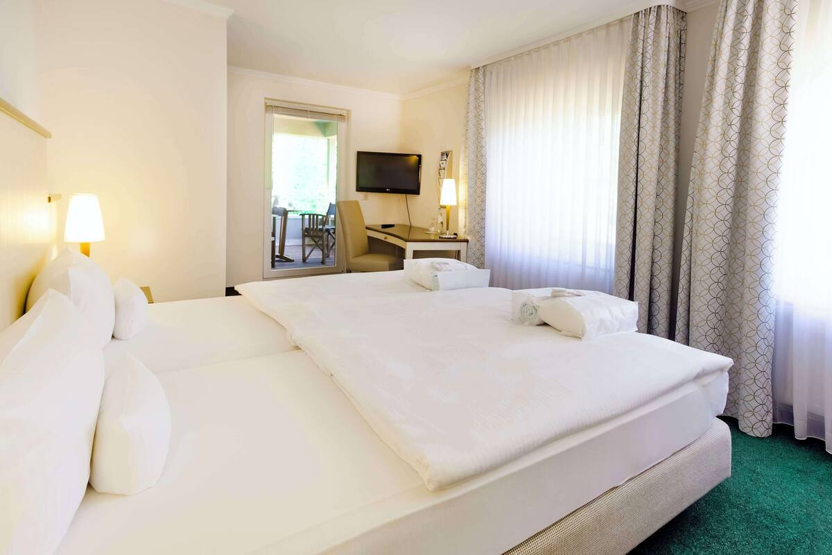 Een hotelkamer met een groot bed, een bureau, een stoel, een televisie en een raam met gordijnen.